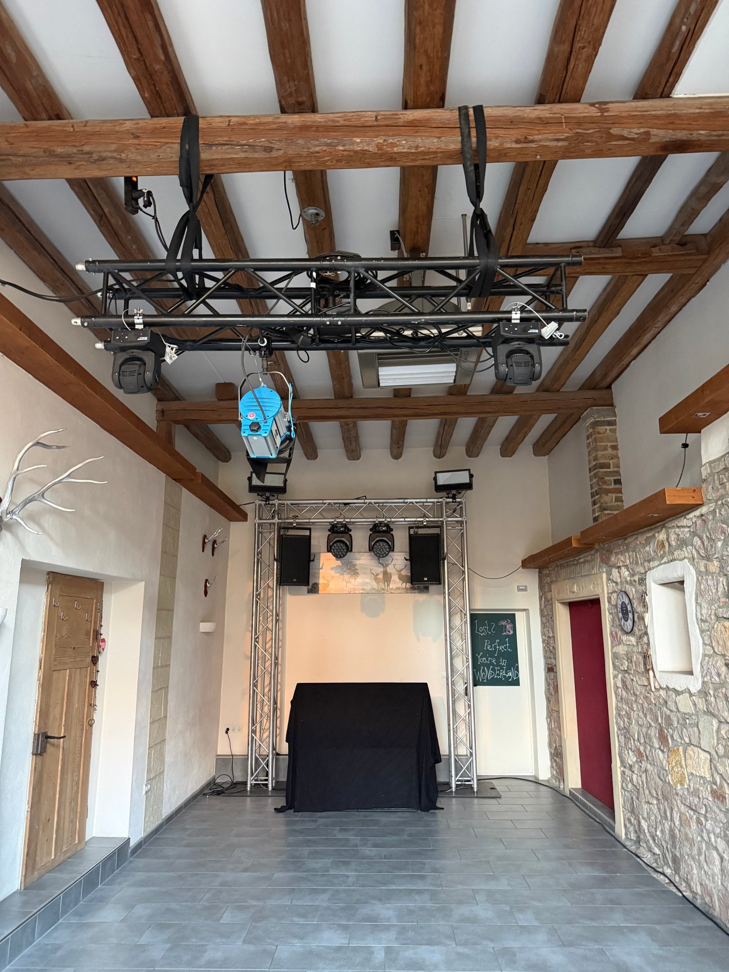 Traversenportal mit DJ-Tisch, Moving Heads und geflogener Traverse unter einer Holzbalkendecke